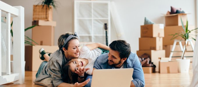 Happy parents and daughter having fun while using laptop and lying down on the floor after moving into new house.