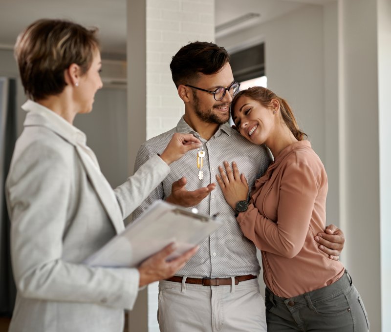 Young happy couple receiving keys of their new home from real estate agent.